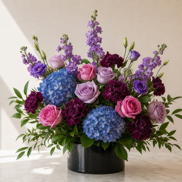 Mixed bouquet of roses, hydrangeas, and purple blooms in a black vase