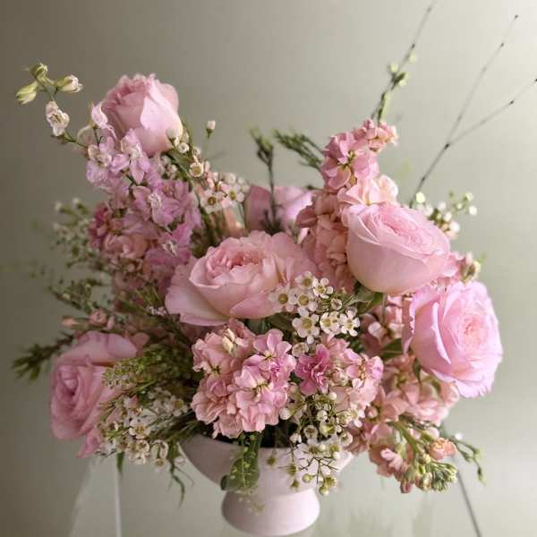 Pink roses and small blossoms arranged in a pale pedestal vase