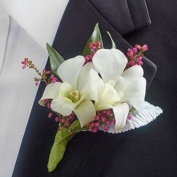 White orchid boutonniere with pink filler flowers on a dark suit lapel