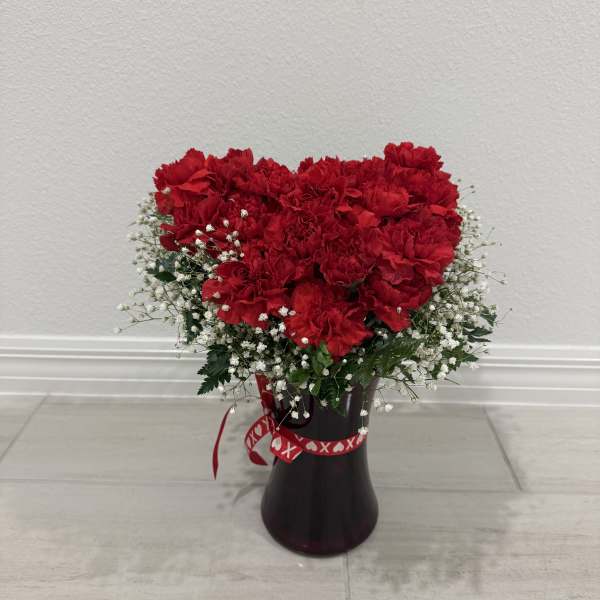 Red carnations arranged in a dark vase with white baby's breath
