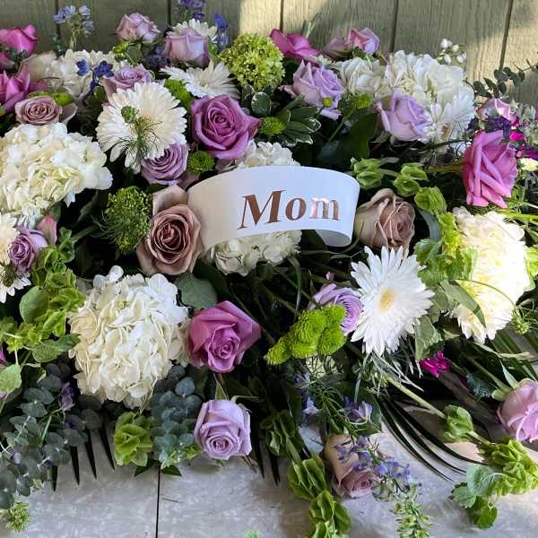 Large floral tribute with pink, lavender, white, and green blooms and a "Mom" card