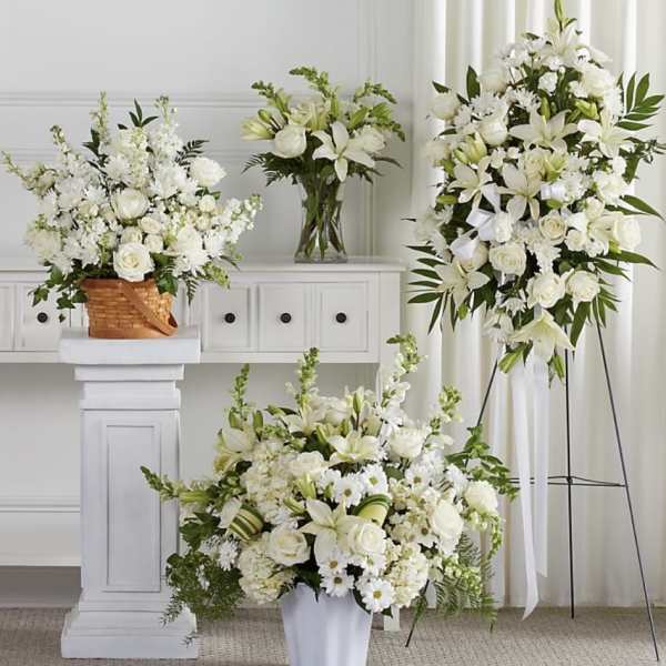 White floral arrangements with lilies and roses in baskets, vases, and a standing spray