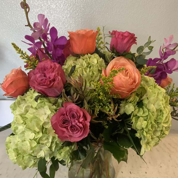 Bouquet of pink and orange roses with green hydrangeas in a glass vase