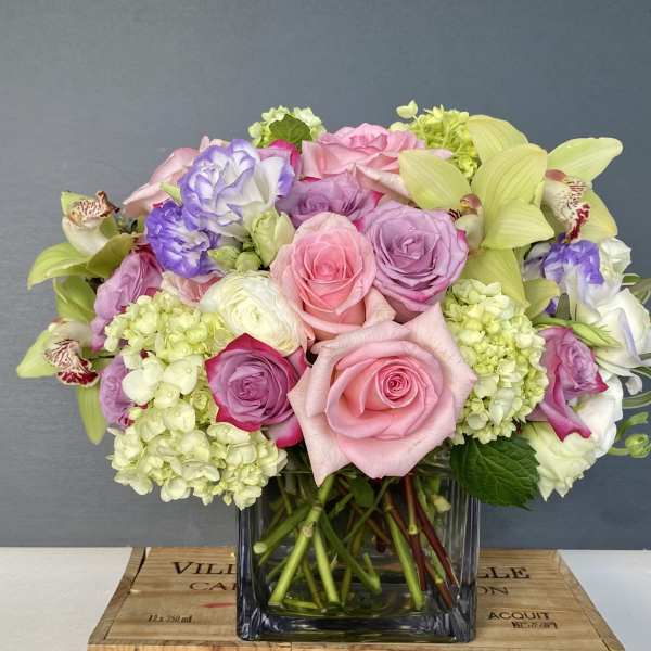 Mixed bouquet of pink and lavender roses with pale green hydrangeas in a glass vase