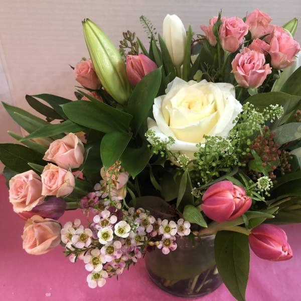 Compact arrangement of white roses, pink spray roses, and tulips in a clear glass vase