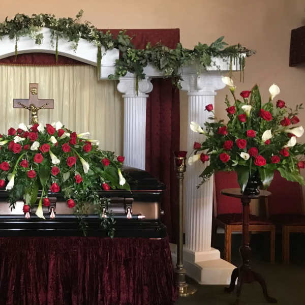 Casket spray and matching rose arrangements around a funeral casket