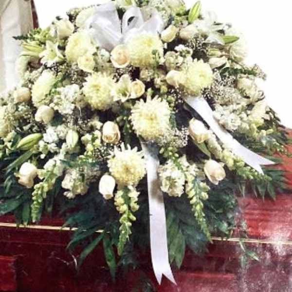 Large white funeral spray with lilies and ribbon on a stand