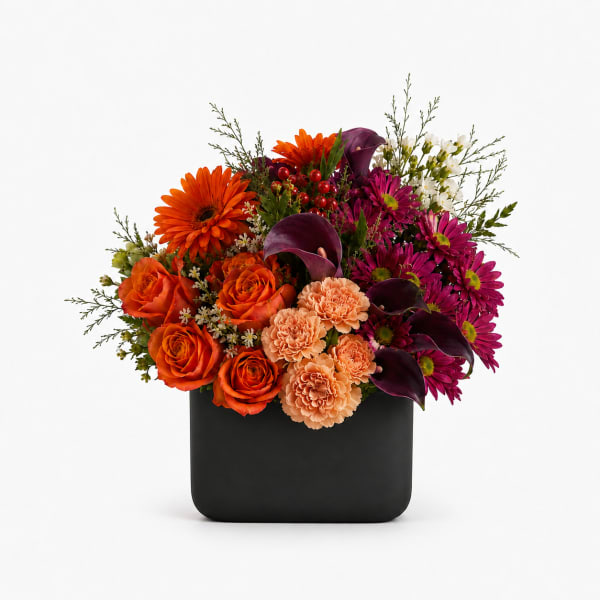 Mixed bouquet of orange, magenta, and peach flowers in a black vase