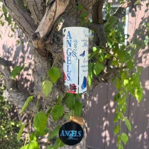 Memorial wind chime with angel-themed text and butterflies hanging from a tree branch