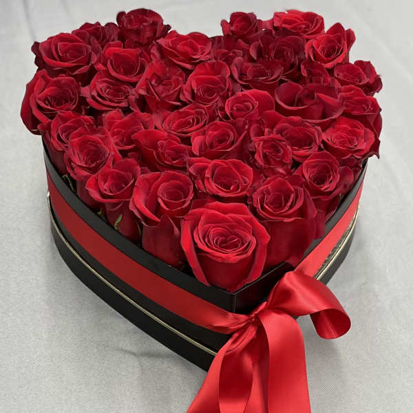 Heart-shaped box filled with red roses and a red satin ribbon