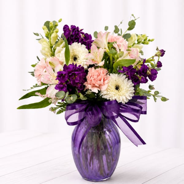 Mixed bouquet of pink, purple, and white flowers in a purple glass vase