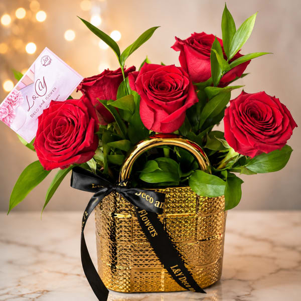 Red roses arranged in a gold basket with a black ribbon