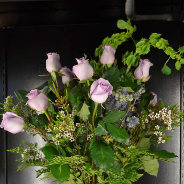 Lavender roses in a clear glass vase with a green ribbon