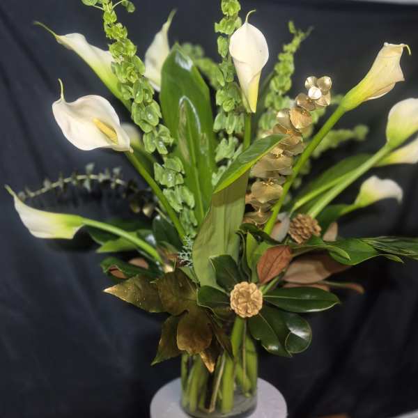 White calla lilies arranged in a clear glass vase with green accents