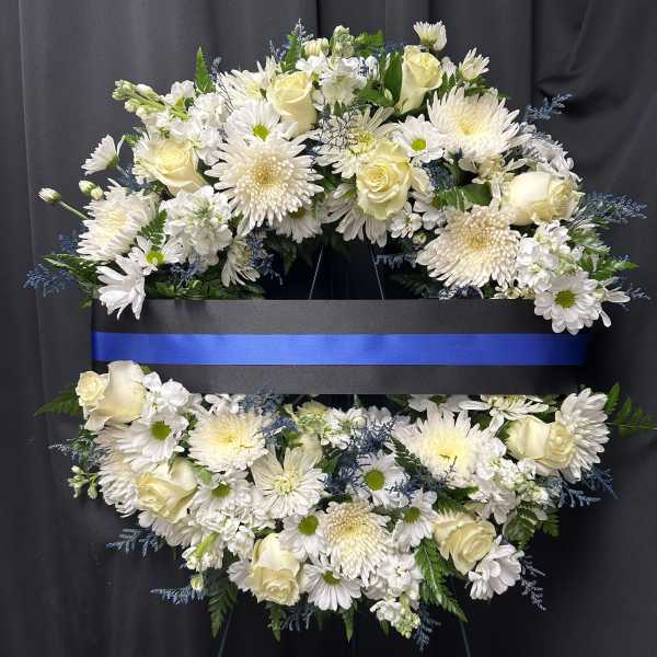 White floral funeral wreath with roses and daisies on a black stand