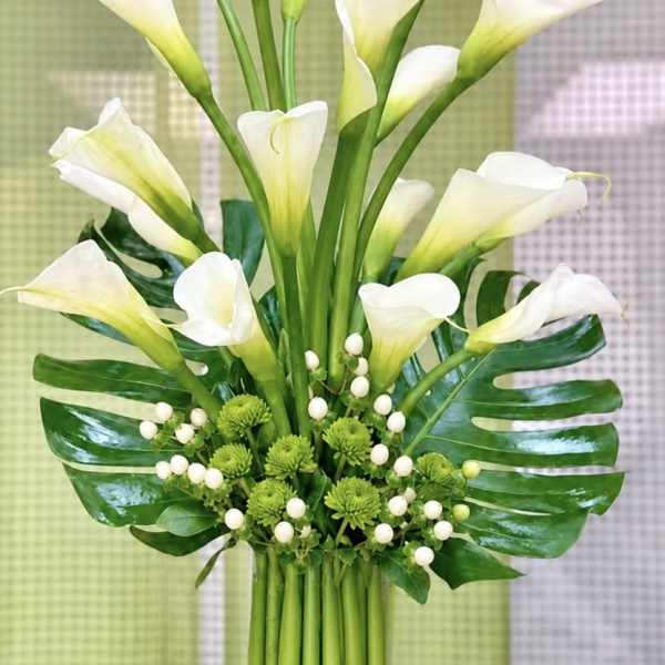 Bouquet of white calla lilies with green accents and tropical leaves