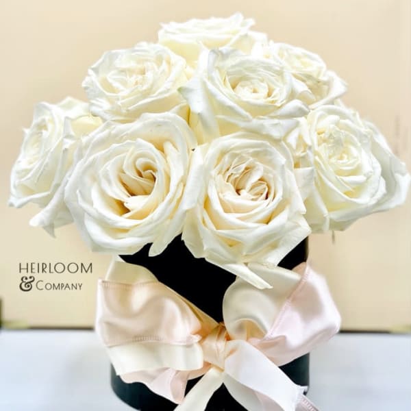 White roses arranged in a black box with a pale satin bow