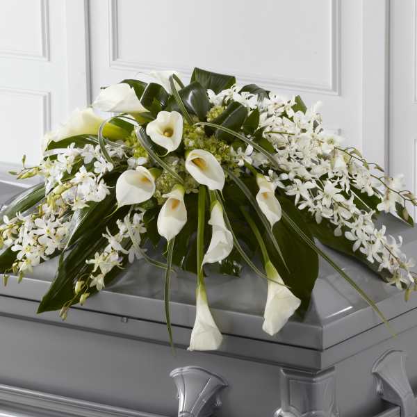 White calla lilies and orchids arranged on a gray casket