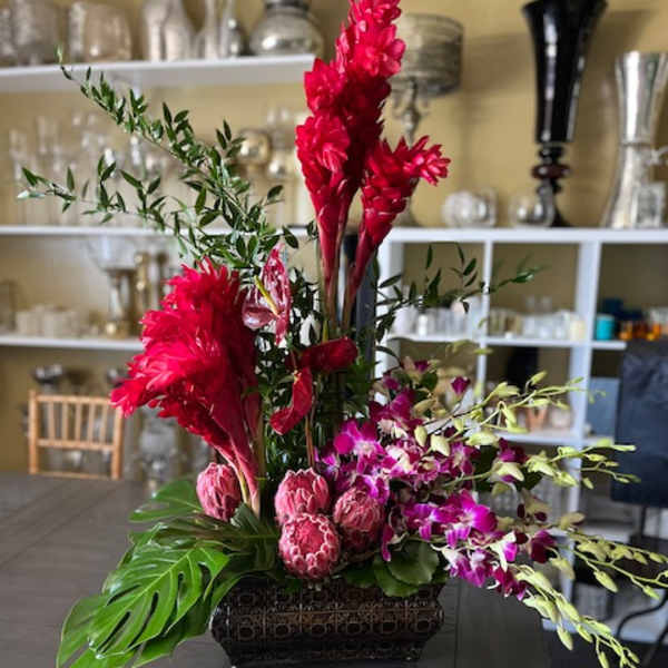 Tropical floral arrangement with red blooms and purple orchids in a dark rectangular vase