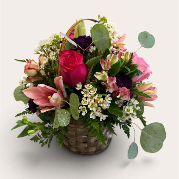 Basket arrangement of pink roses, lilies, and small white flowers