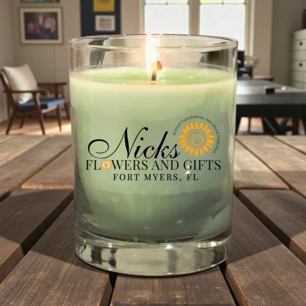Green candle in a clear glass tumbler with a lit wick