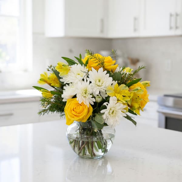 Yellow roses and white daisies in a clear glass vase