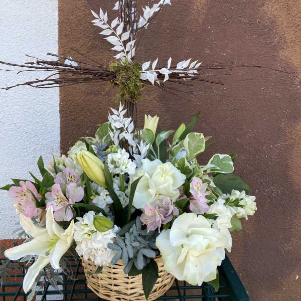 White and pale pink floral arrangement in a wicker basket with a tall cross centerpiece