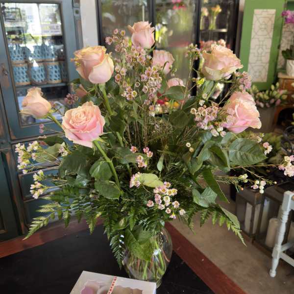 Pink roses and tiny pink filler flowers in a glass vase with a box of chocolates
