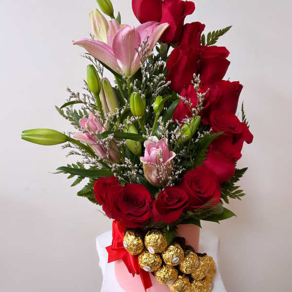Red roses and pink lilies in a pink vase with gold-wrapped chocolates