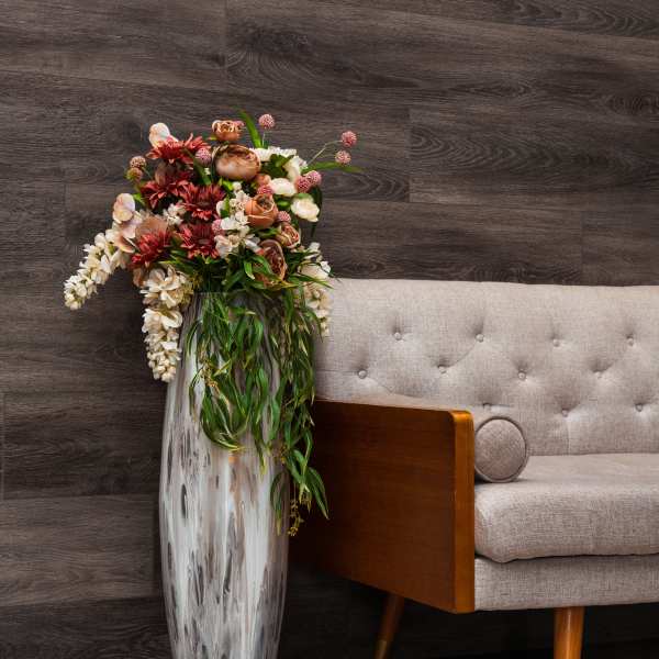 Tall floral arrangement in a silver vase beside a beige sofa