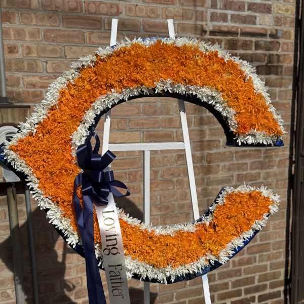 Orange and white floral funeral wreath on a stand with a ribbon