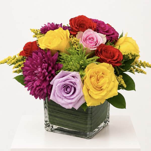 Colorful bouquet of roses and purple mums in a square glass vase