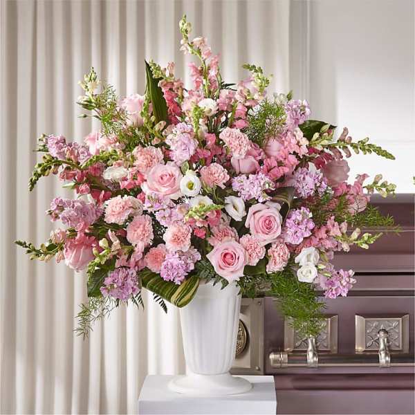 Pink and white floral arrangement in a white urn beside a casket