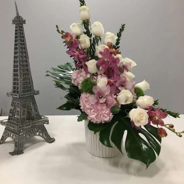 Pink and white floral arrangement in a white vase beside a small Eiffel Tower model