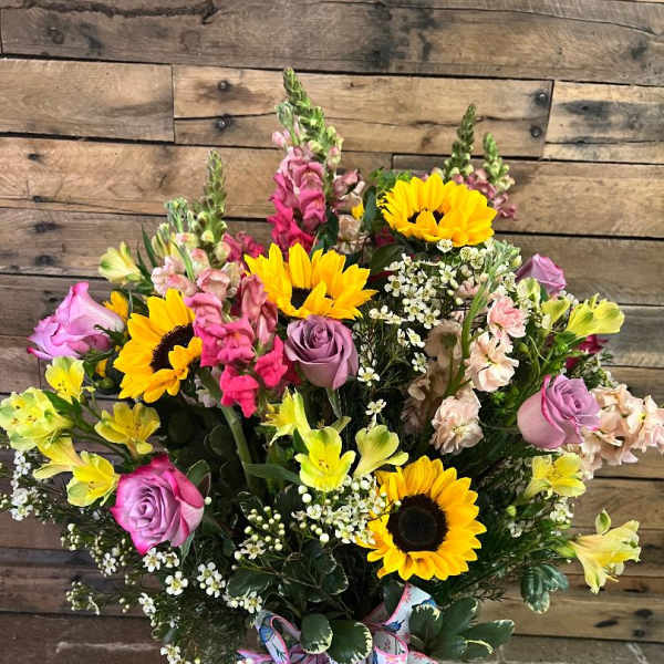 Bouquet of sunflowers, pink roses, and mixed blooms in a glass vase