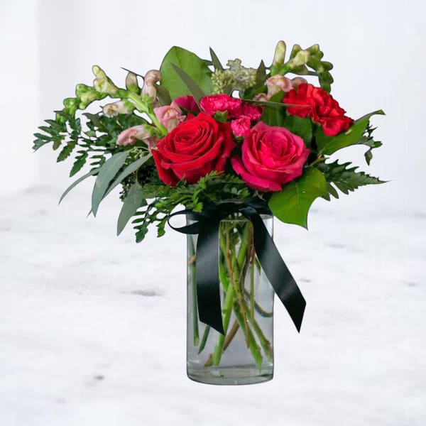Bouquet of red and pink roses in a clear glass vase with a black ribbon