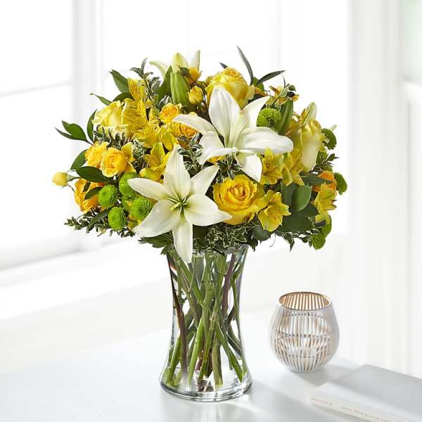 Yellow and white bouquet of lilies and roses in a clear glass vase
