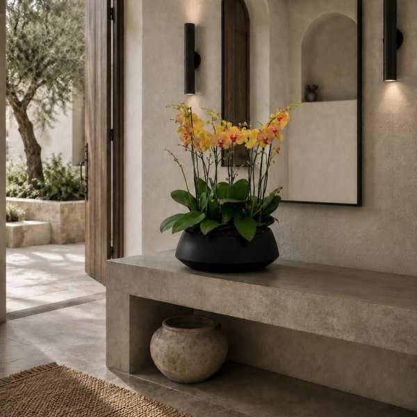Orange and yellow orchids in a black bowl on a stone console