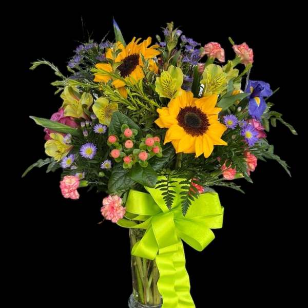 Bouquet of sunflowers, alstroemeria, and purple daisies in a glass vase with a lime ribbon