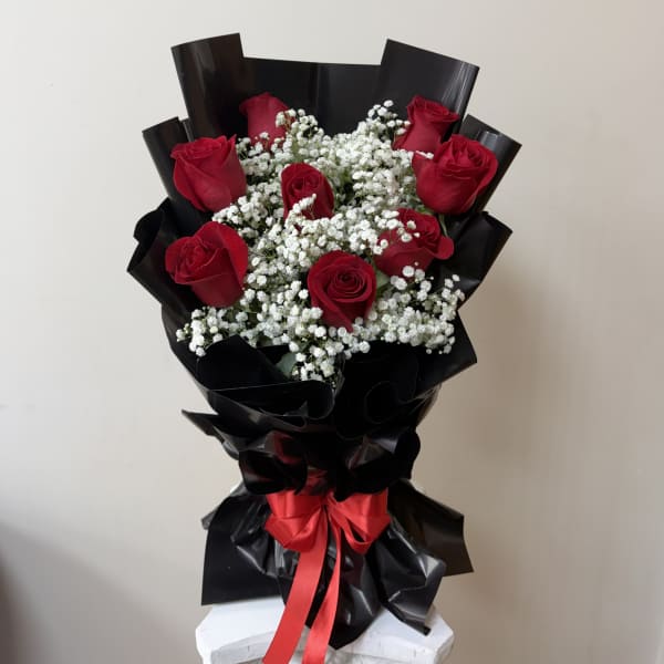 Bouquet of red roses and white baby's breath wrapped in black paper with a red ribbon