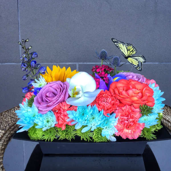 Colorful mixed flower arrangement in a black rectangular container with butterfly picks