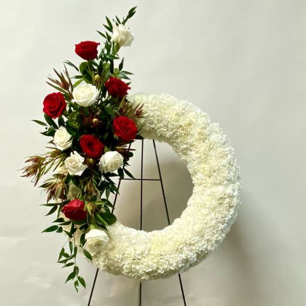 White floral wreath with red and white roses on a stand