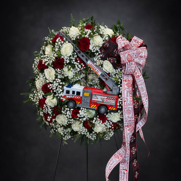 Firefighter-themed rose wreath with a toy fire truck and ribbon on a stand
