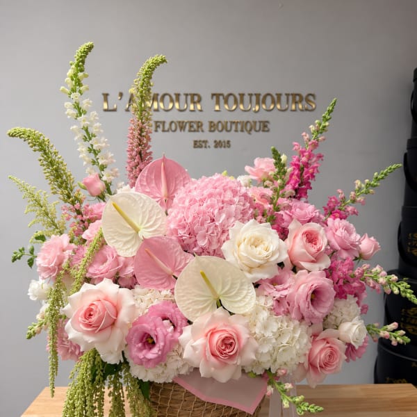 Pink and white floral arrangement in a wicker basket with ribbon