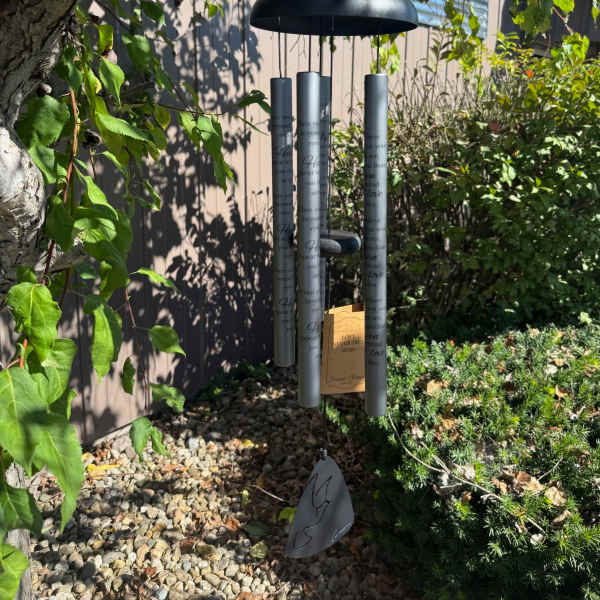 Black memorial wind chime hanging outdoors among trees and shrubs