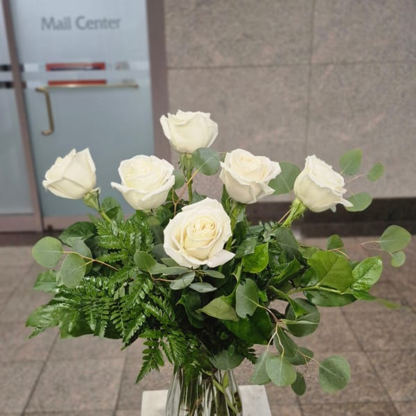 White roses in a clear glass vase with mixed greenery
