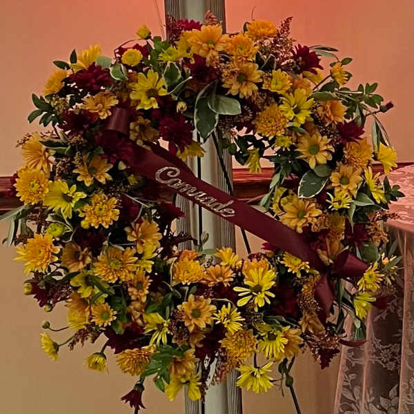 Large floral funeral wreath with yellow and burgundy daisies and a memorial ribbon