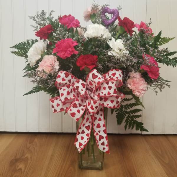 Heart-themed bouquet of pink, red, and white carnations in a glass vase