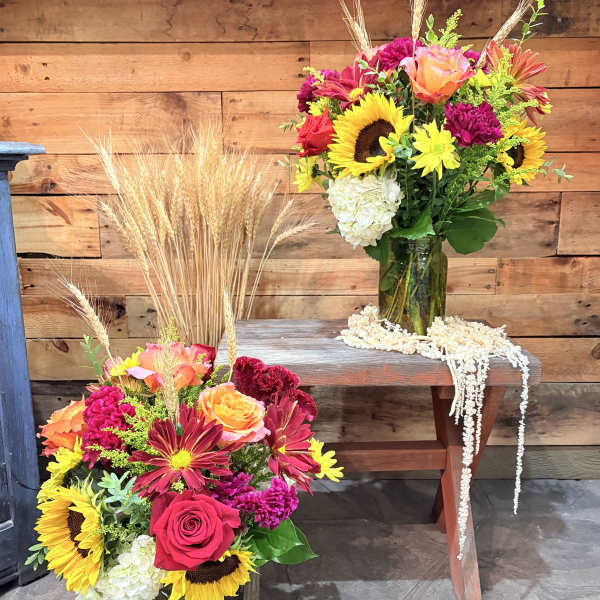 Two colorful flower arrangements in green glass vases with wheat accents