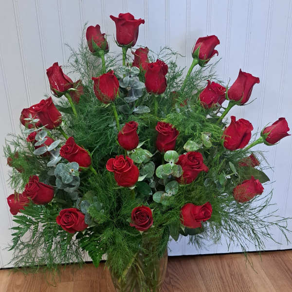 Red roses arranged in a clear glass vase with airy greenery